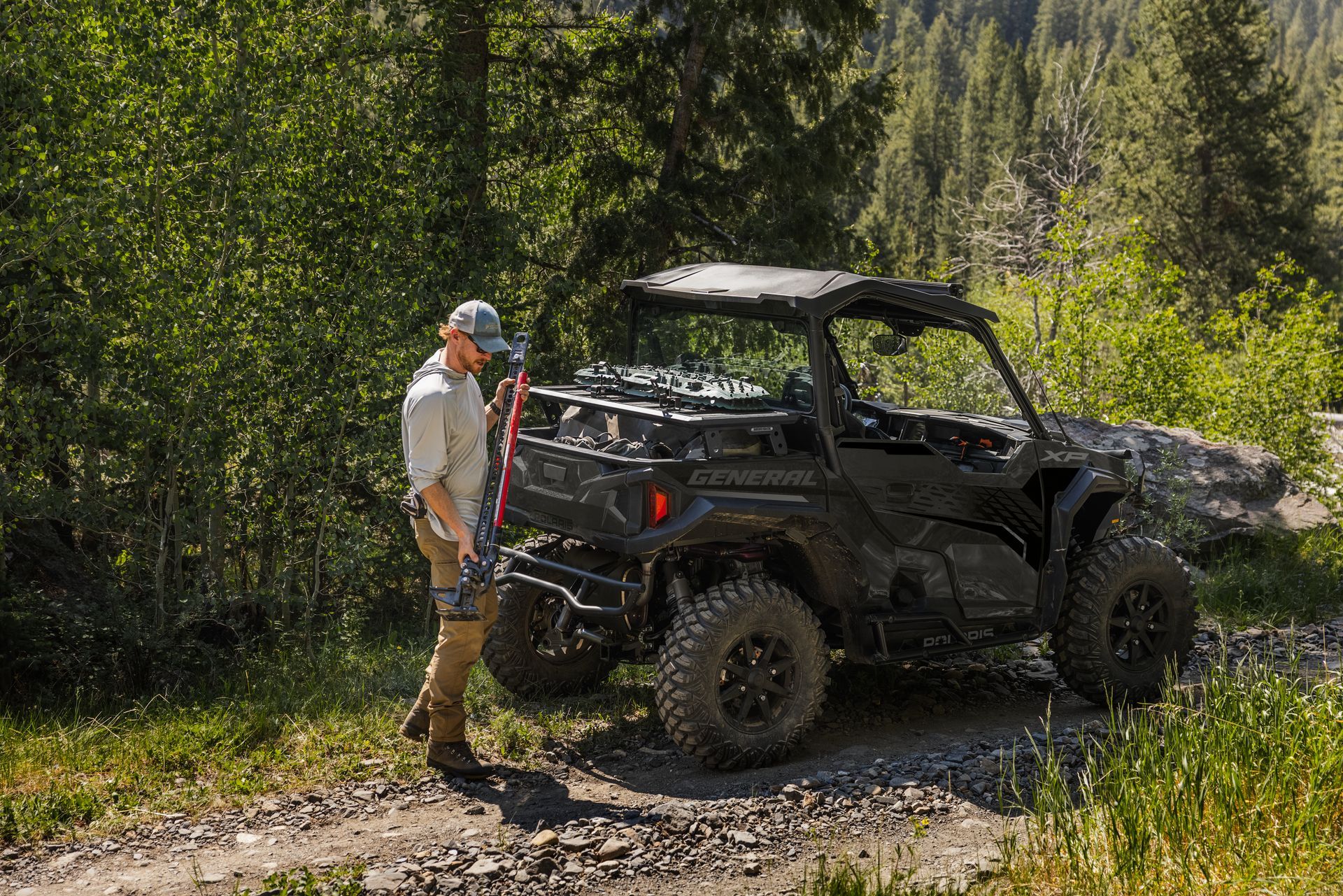 A man is standing next to a polaris utility vehicle on a dirt road.