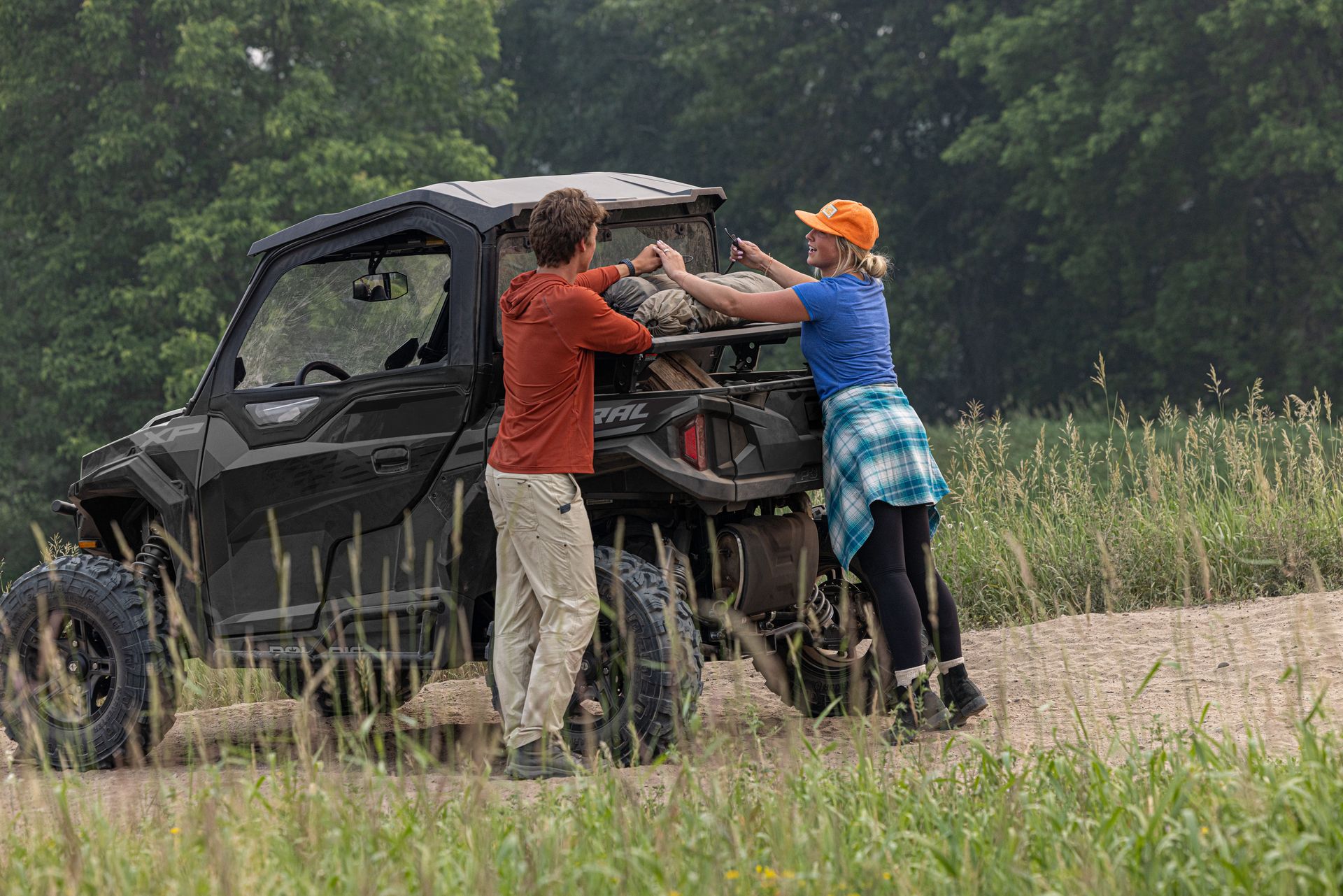 A man and a woman are pushing a atv down a dirt road.