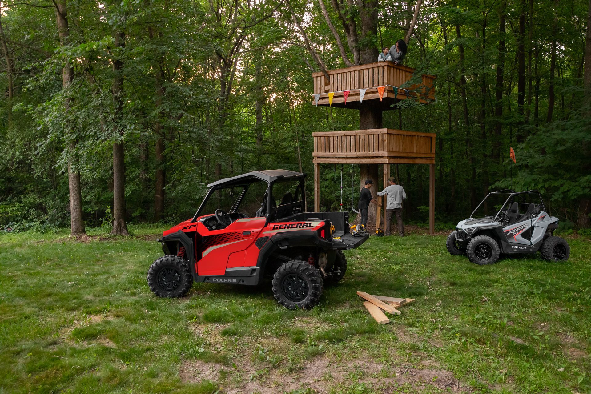 Two atvs are parked in a grassy field next to a tree house.