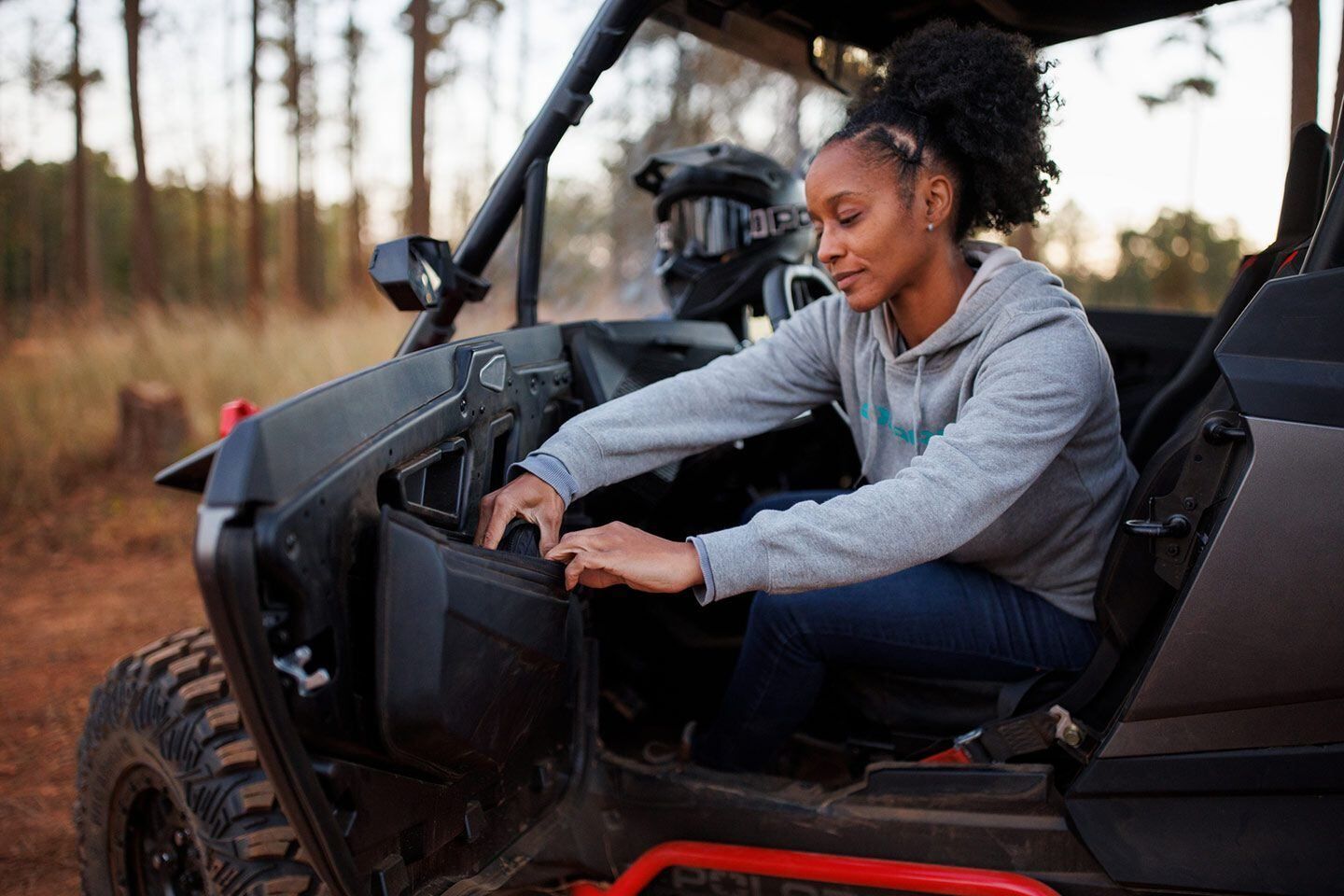 A woman is sitting in a atv in the woods.