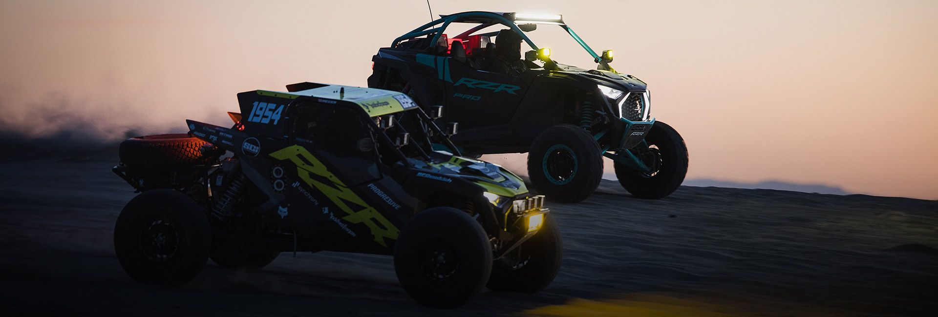 Two atvs are racing on a dirt road at sunset.