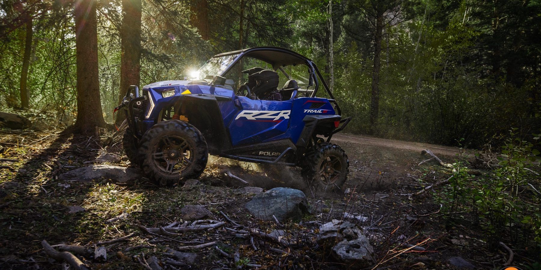 A blue atv is driving down a dirt road in the woods.