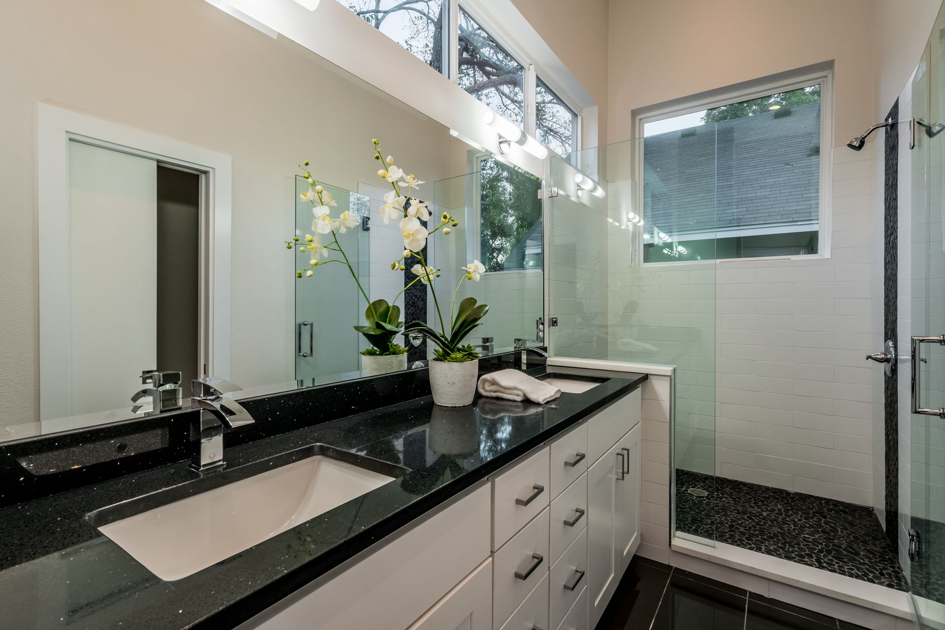 Modern bathroom with white cabinets, a black countertop with a white sink, a large mirror, and a glass-enclosed shower.
