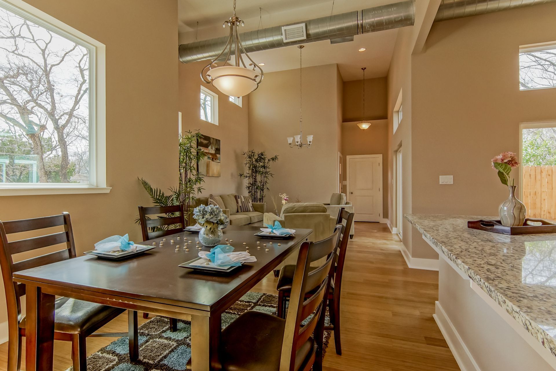 A dining area with a dark wood table set for four, adjacent to an open kitchen with a granite countertop and neutral decor.