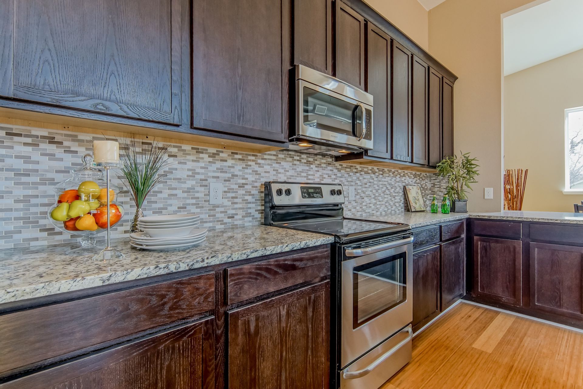 A modern kitchen featuring dark wood cabinets, stainless steel appliances, speckled granite countertops, and tile backsplash.