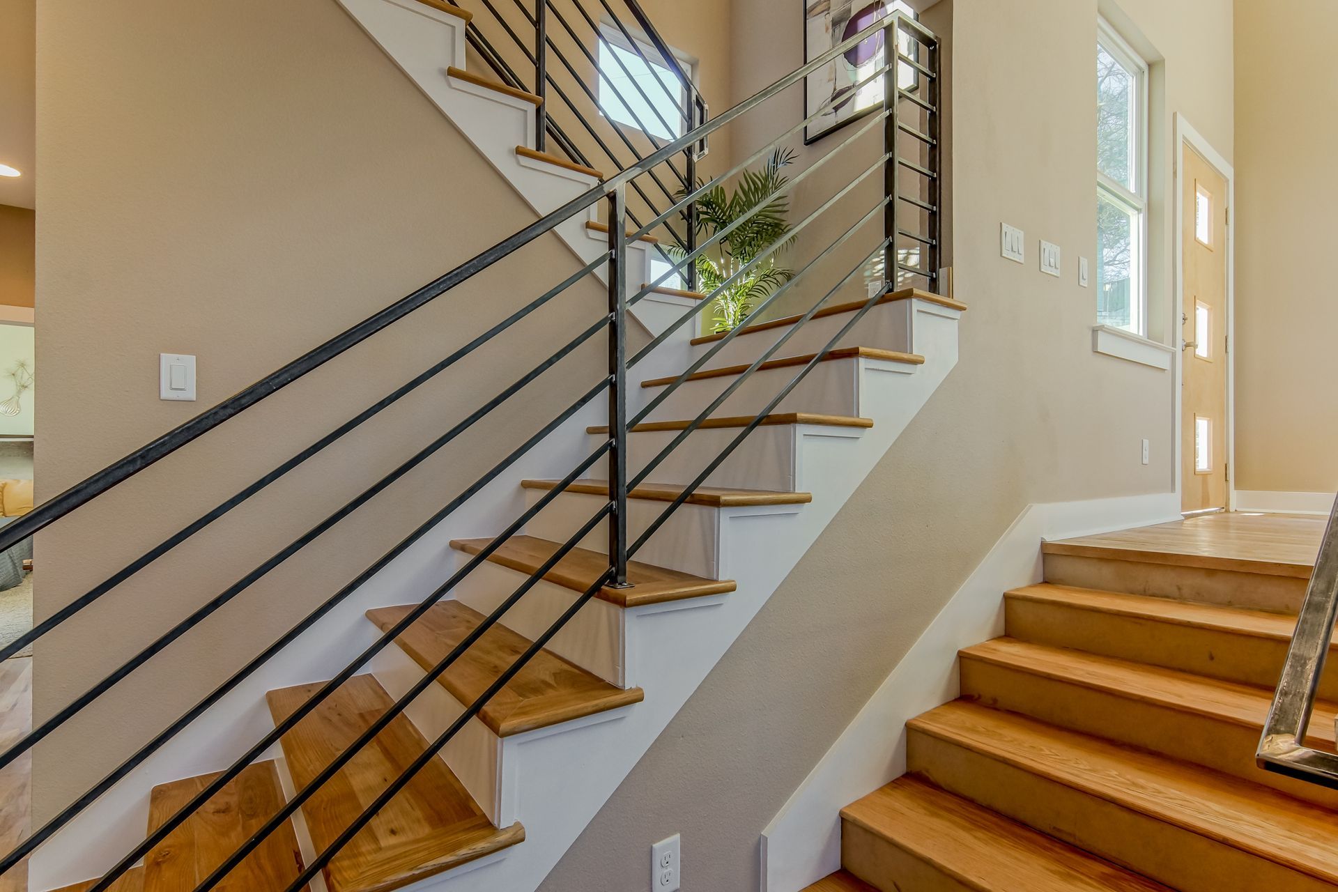 A staircase with light wood steps, white risers, and a modern black metal railing in a neutrally colored hallway.