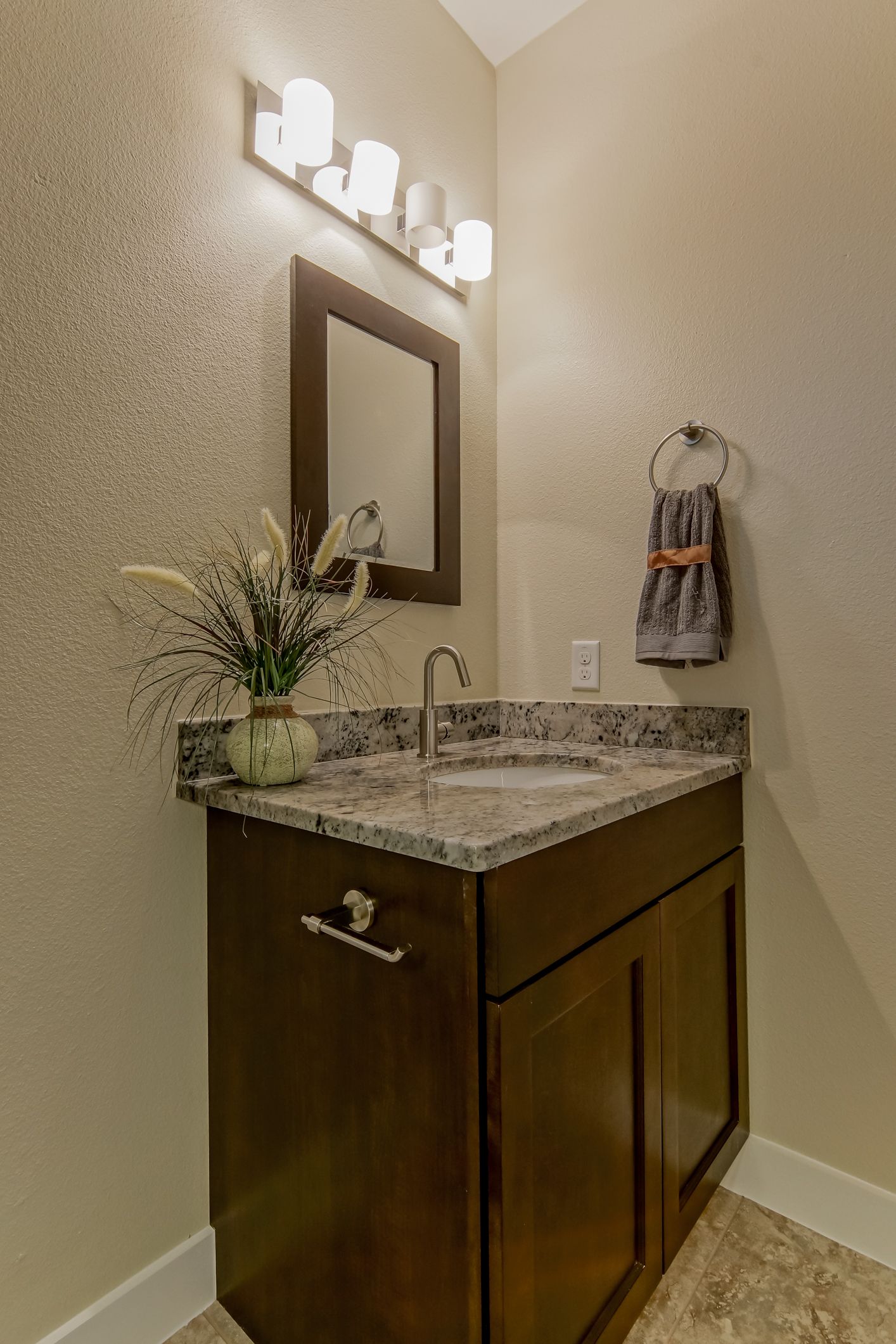 Small bathroom vanity with a dark wood cabinet, granite countertop, mirror, light fixture, and a hand towel.
