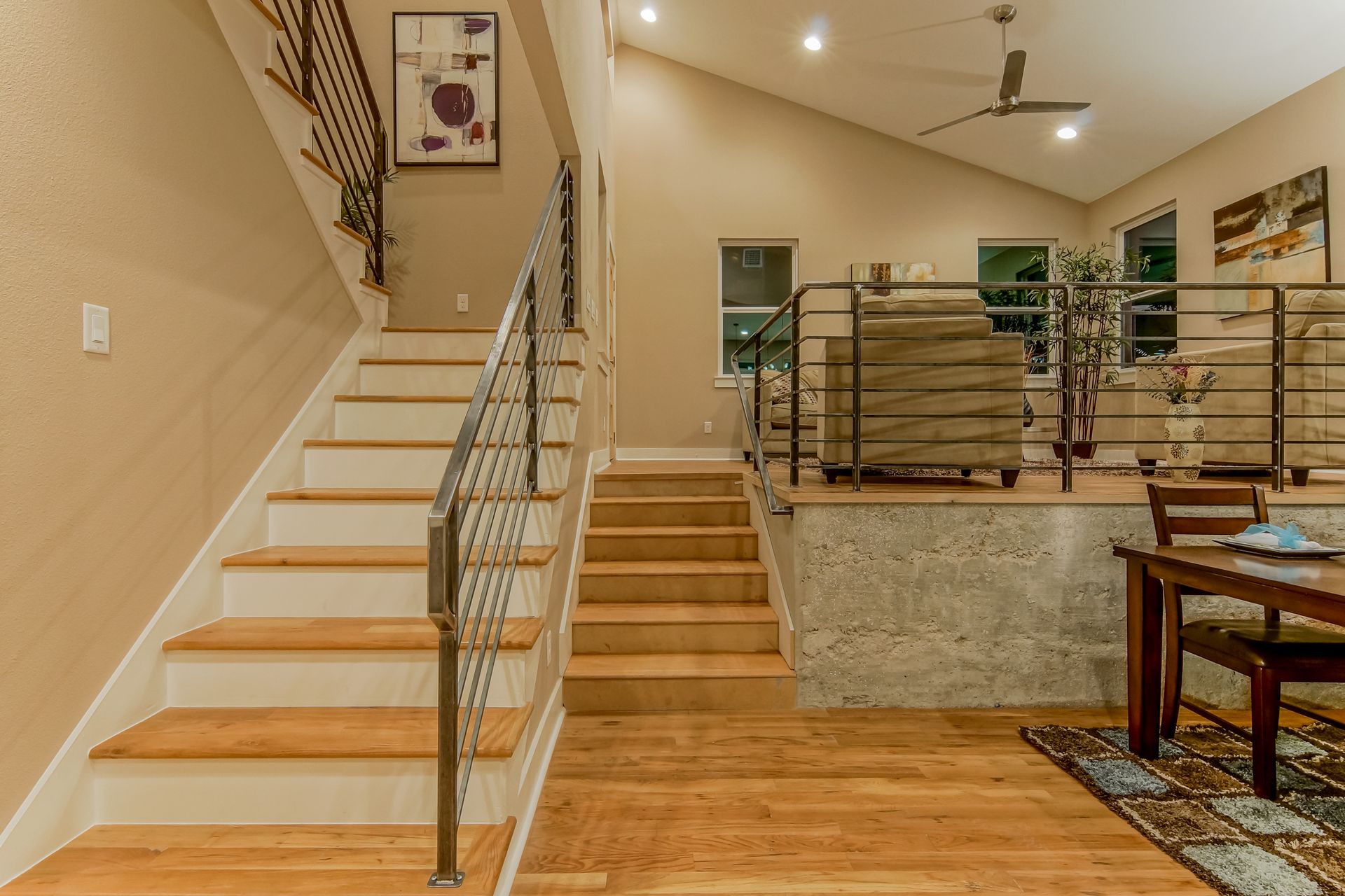 A room with wood-floored stairs leading to a raised living area with light walls and furniture, framed by metal railings.