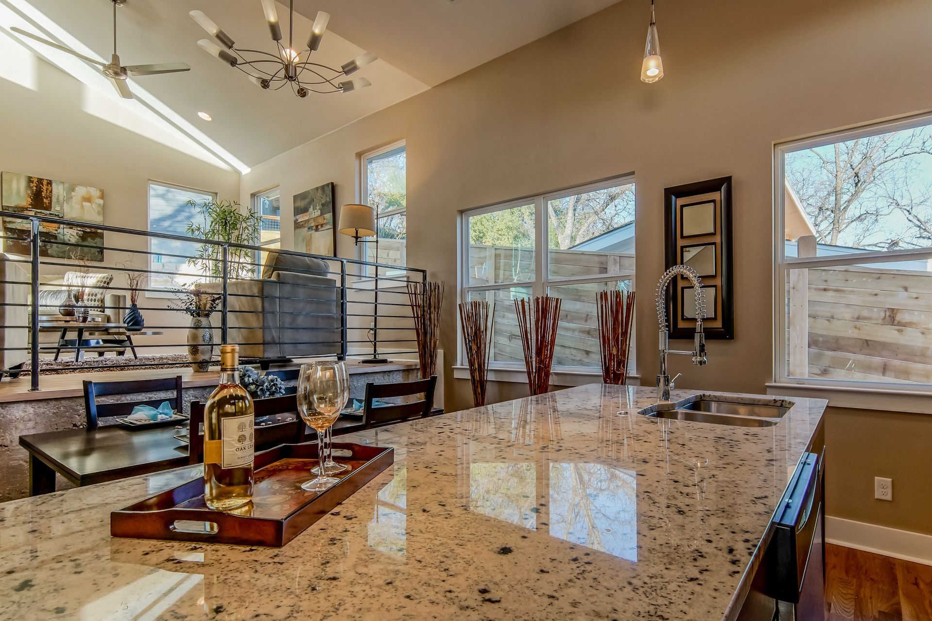 A granite kitchen island with a wine bottle and glass on a tray, featuring high ceilings and windows in the background.