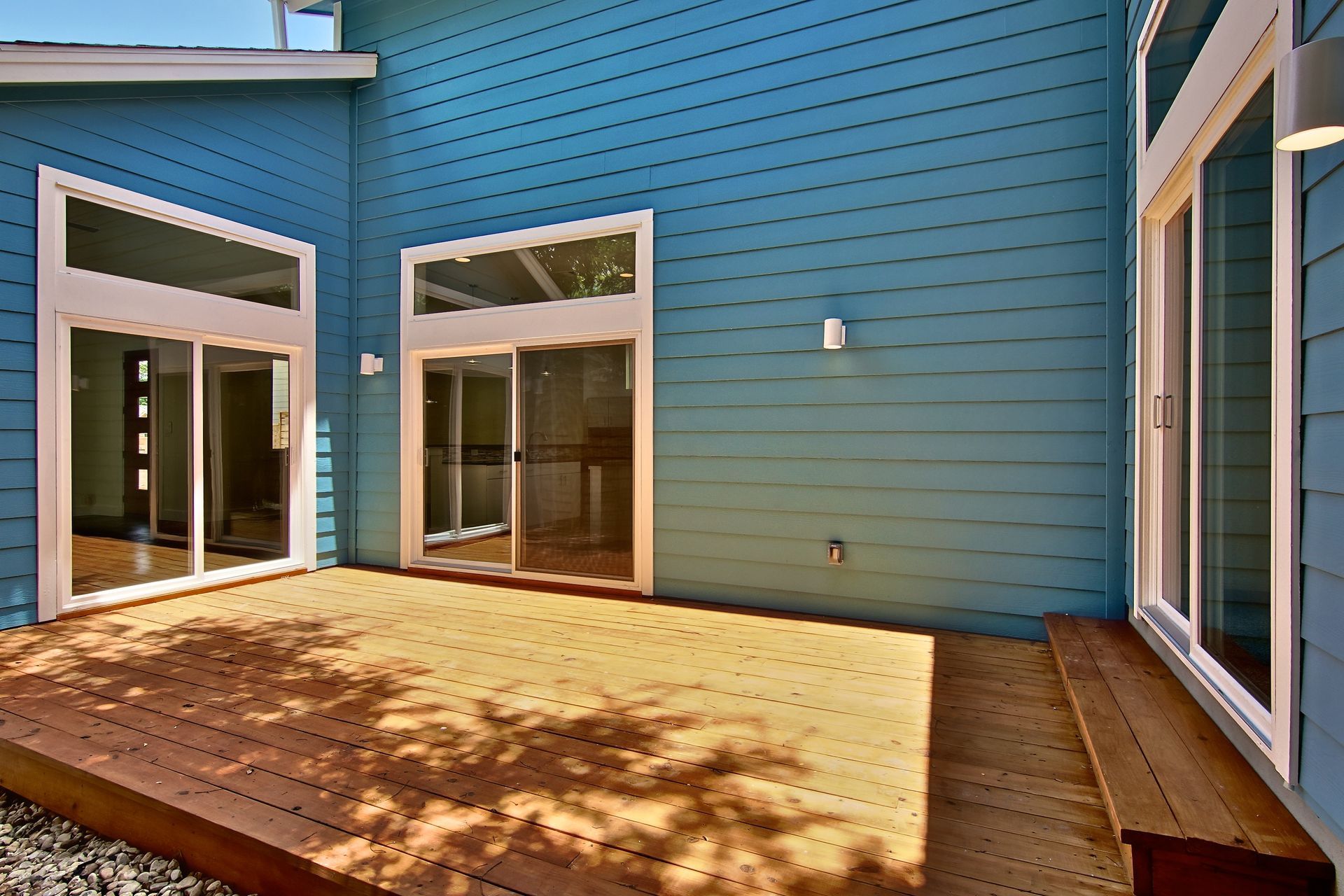 A wooden deck leads to sliding glass doors on a house with blue horizontal siding.