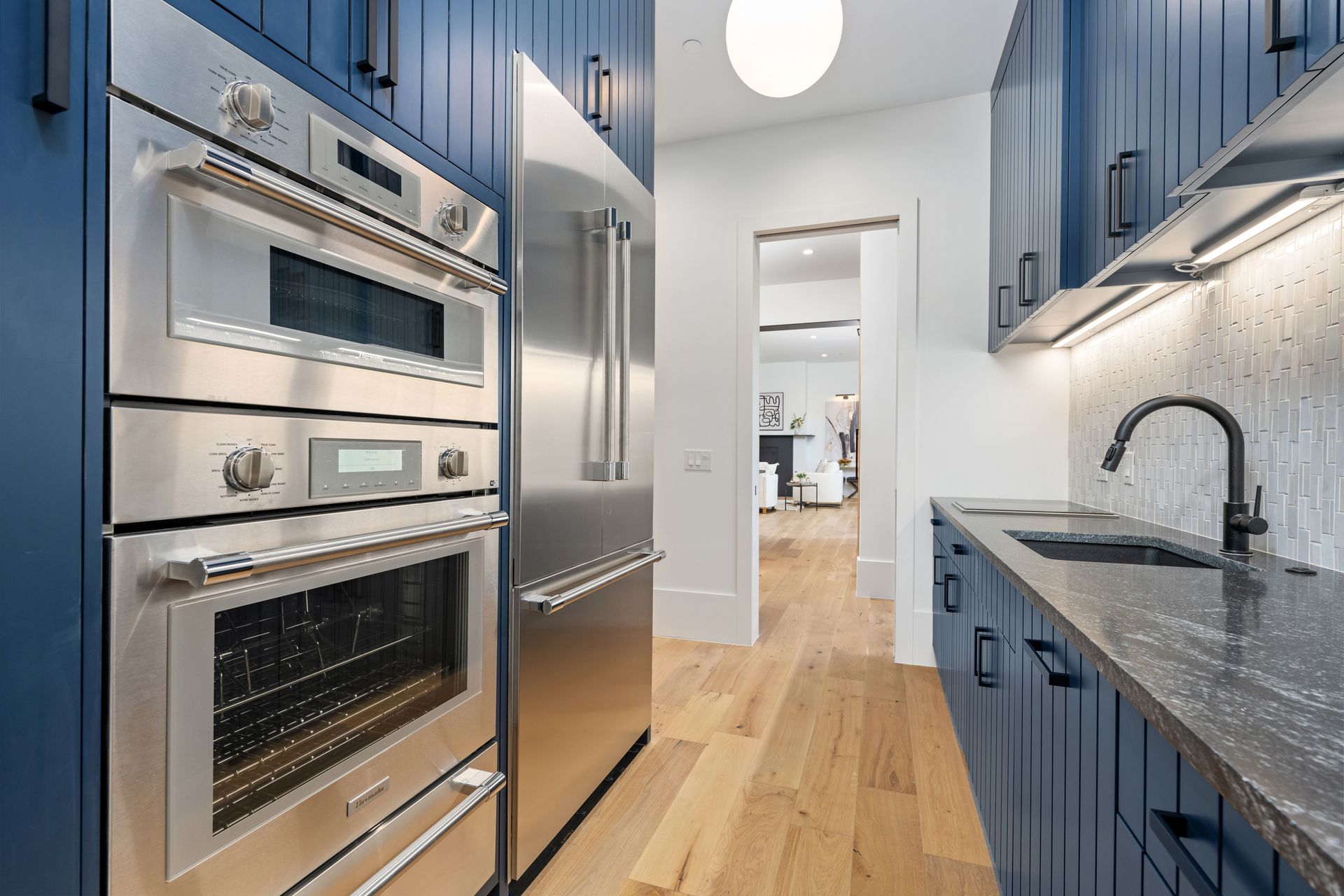 Modern kitchen with navy blue vertical-plank cabinets, stainless steel double wall ovens, refrigerator, and granite top.