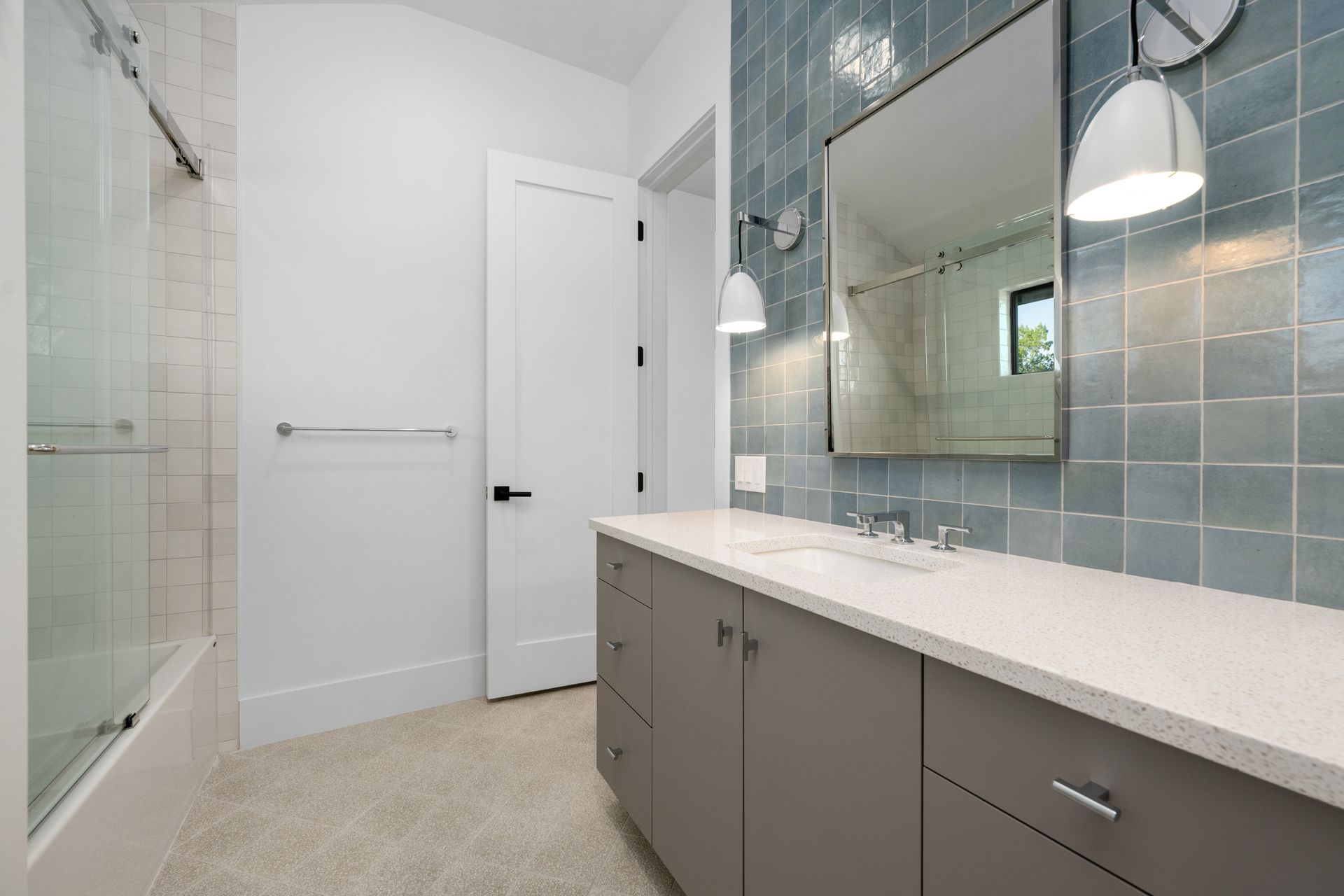 Modern bathroom with a grey vanity, white quartz countertop, blue-tiled accent wall, and a walk-in glass shower.