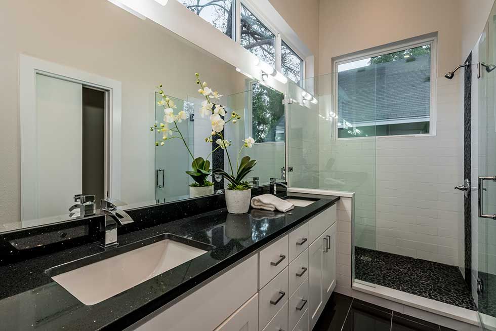 Modern bathroom with a black granite countertop, white vanity cabinets, large mirror, and a glass-enclosed shower.
