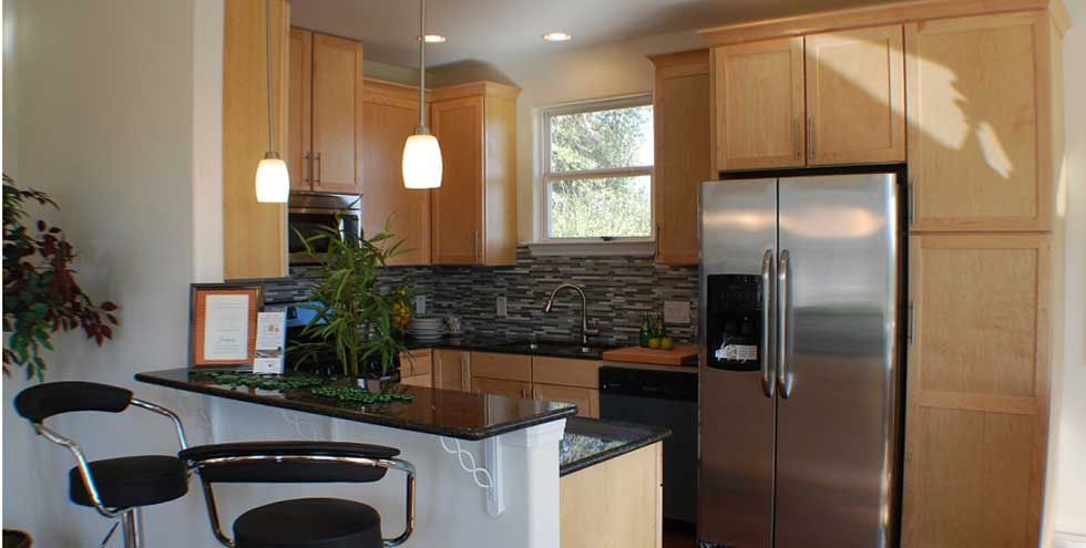 A modern kitchen featuring light wood cabinets, stainless steel appliances, a tiled backsplash, and a black bar counter.