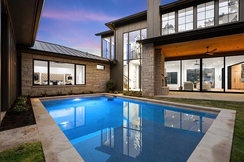 A modern two-story home with stone siding and a blue rectangular swimming pool in the backyard at sunset.