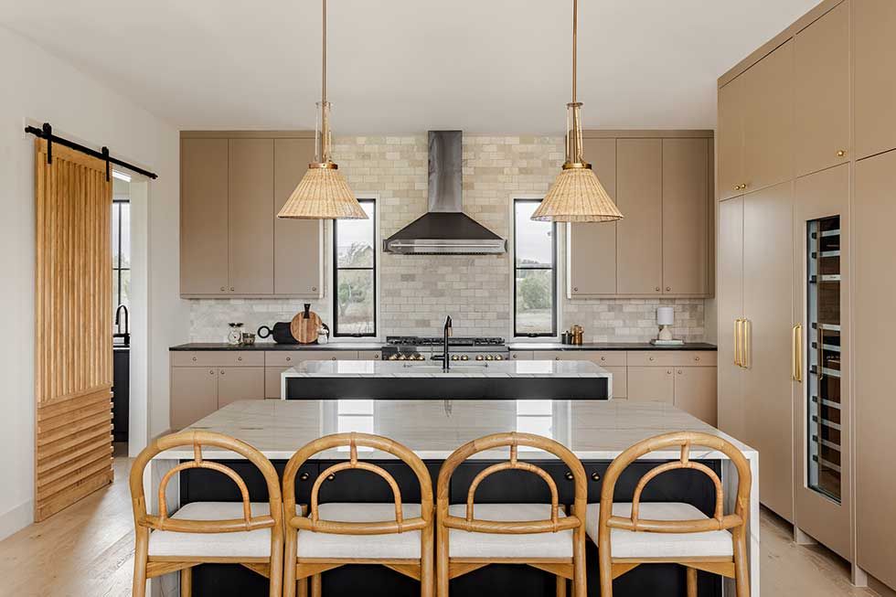 Modern kitchen with light wood cabinets, two center islands, rattan bar stools, and stone backsplash with a range hood.