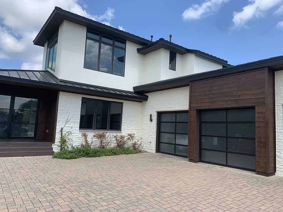 Modern two-story house with white stucco, textured stone siding, dark wood accents, and a paved driveway.