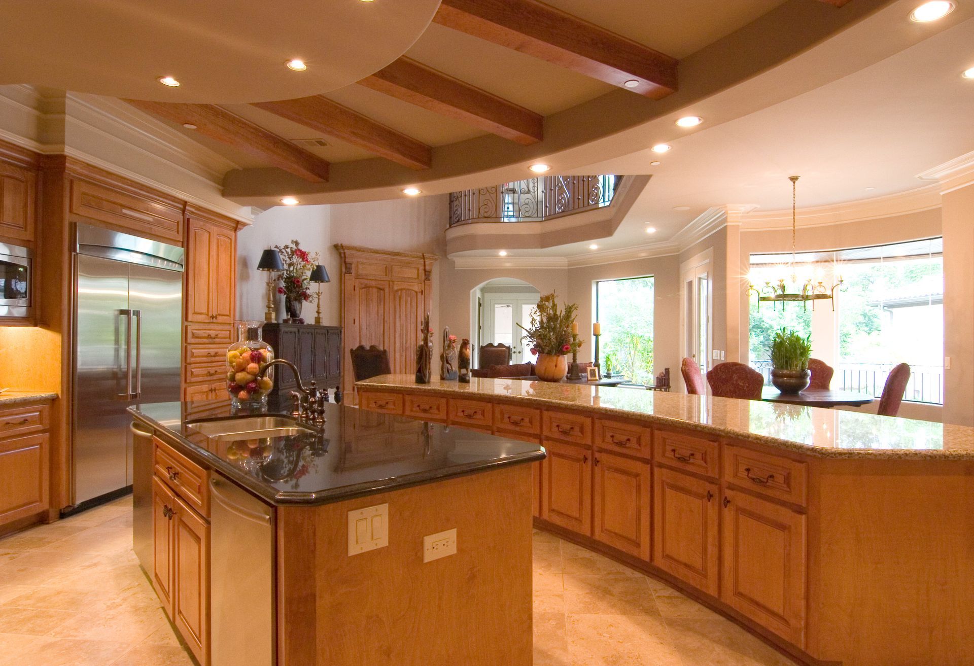 A large, upscale kitchen featuring wood cabinets, a black granite island, and a dining area with views of greenery.