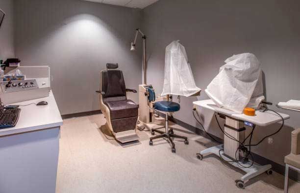 An exam room featuring an adjustable medical chair, an examination stool, and diagnostic equipment covered in plastic.