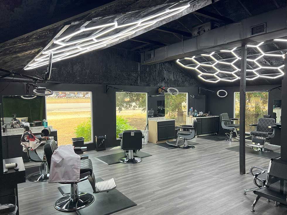 Modern barbershop interior with black walls, gray wood floors, barber chairs, and geometric LED ceiling lighting.