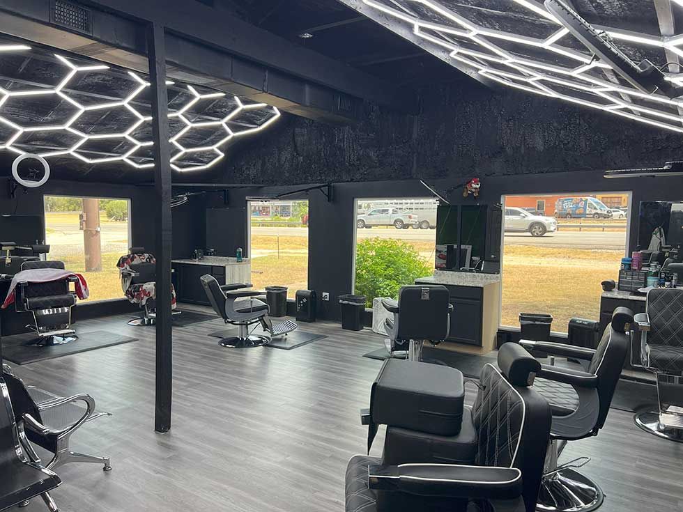 A modern barbershop with dark walls, grey flooring, multiple barber chairs, and a geometric LED ceiling light fixture.