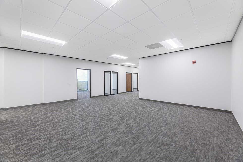 An empty office space with white walls, gray carpet, drop ceiling lights, and several doorways leading to other rooms.