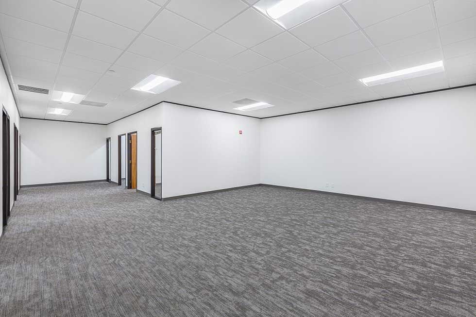 Empty office suite with white walls, gray carpeted floors, and recessed ceiling lights.