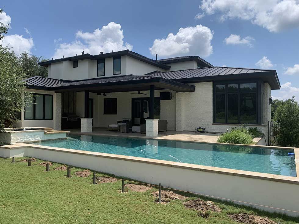 A modern white house with a dark metal roof and a spacious covered patio overlooking a rectangular swimming pool.
