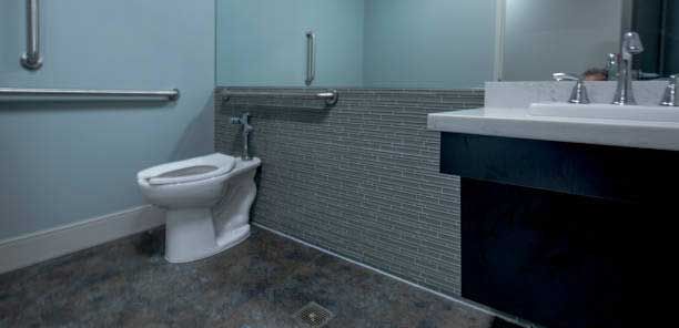 An accessible restroom featuring a white toilet, horizontal grab bars, and a modern vanity with a sink.