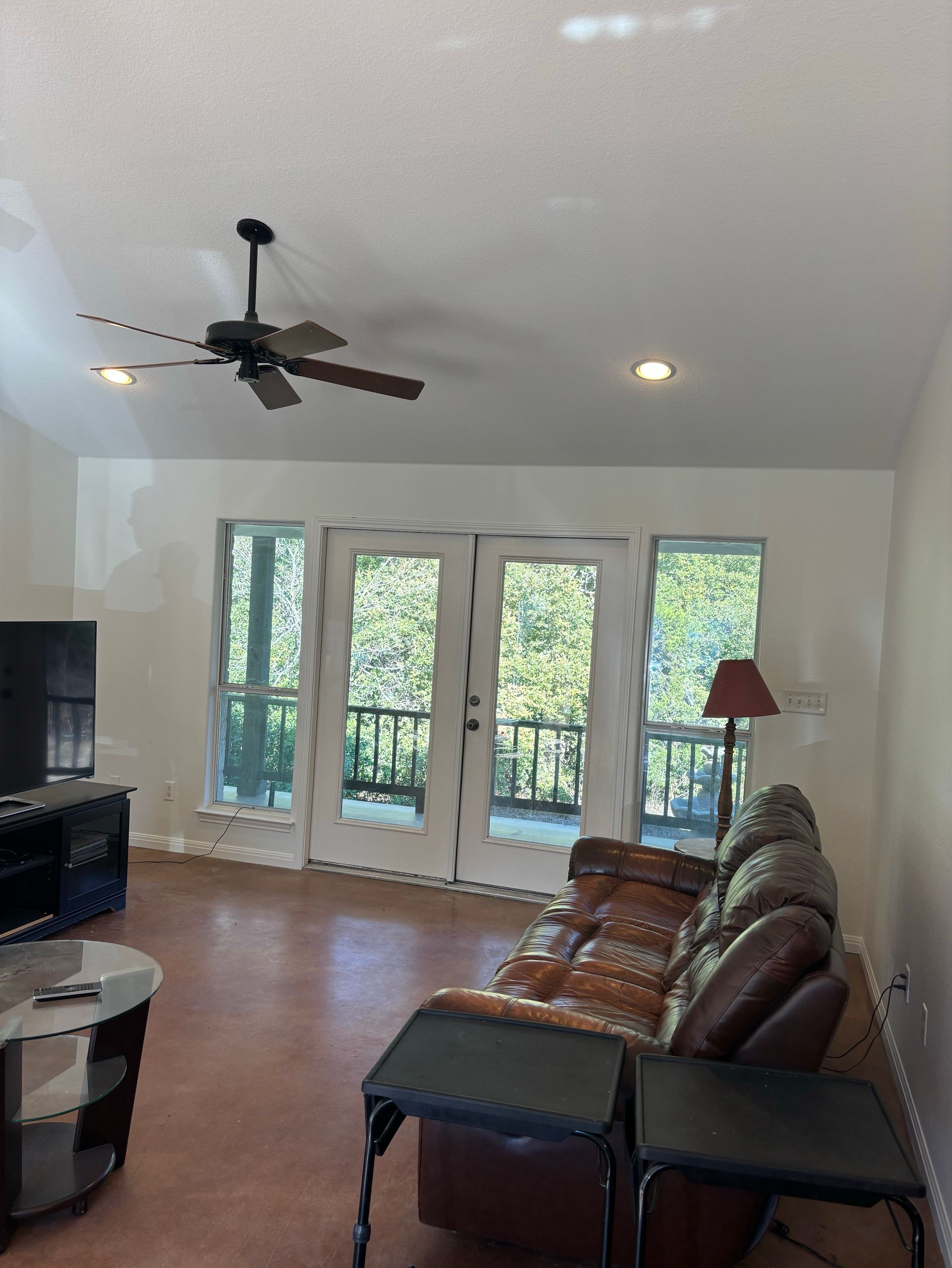 A living room with light walls, a vaulted ceiling with a fan, double glass doors to a deck, and a brown leather sofa.
