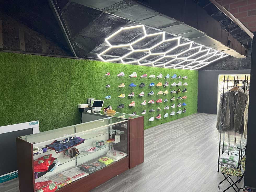 A shoe store with sneakers displayed on a green grass wall, a glass checkout counter, and geometric ceiling lights.