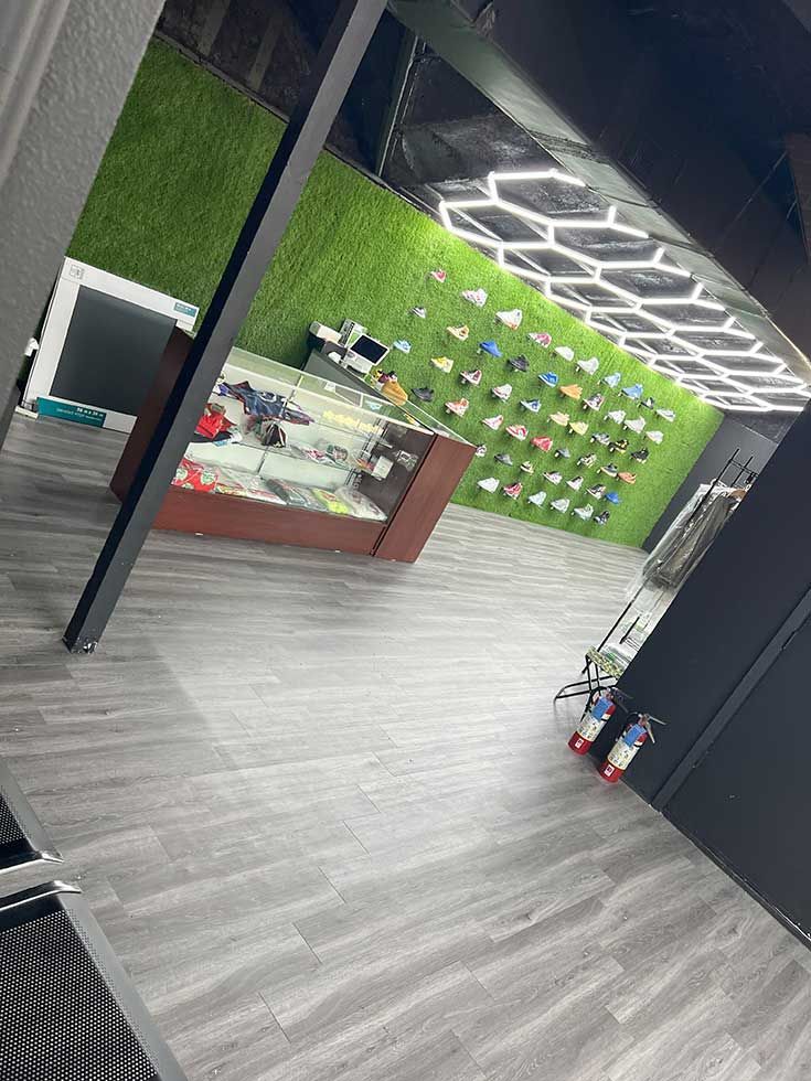 A sneaker store interior with grey wood floors, a green wall displaying footwear, and a glass service counter.