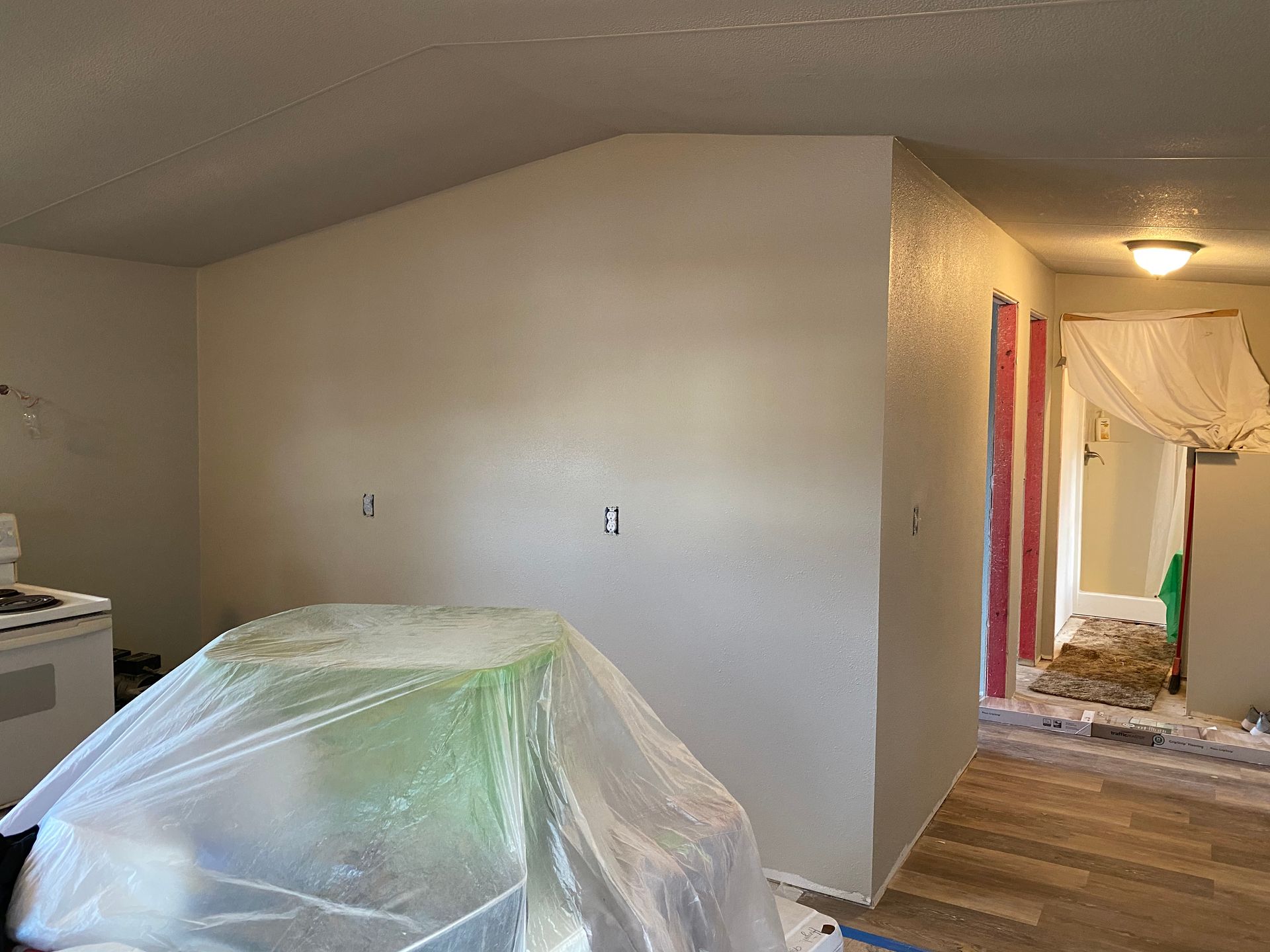Room with freshly painted light-colored walls; furniture covered in plastic; doorway visible.