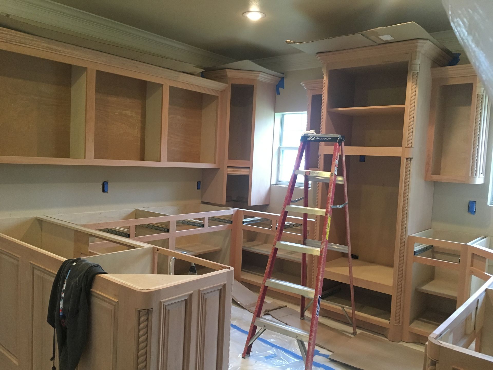 Kitchen cabinets in various stages of construction; a red ladder stands near a window.