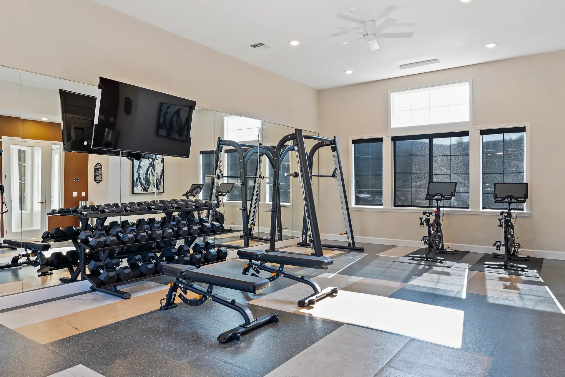 A large gym with a lot of dumbbells and a tv on the wall.