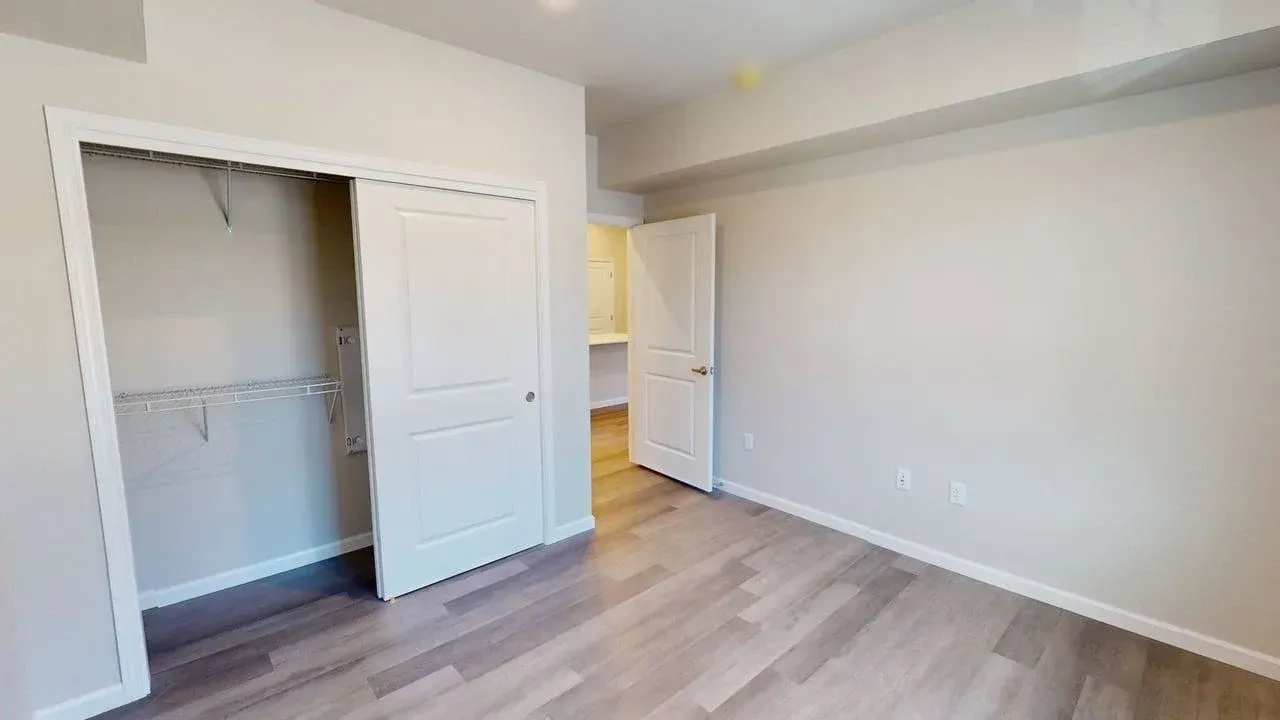 An empty bedroom with a walk in closet and hardwood floors.