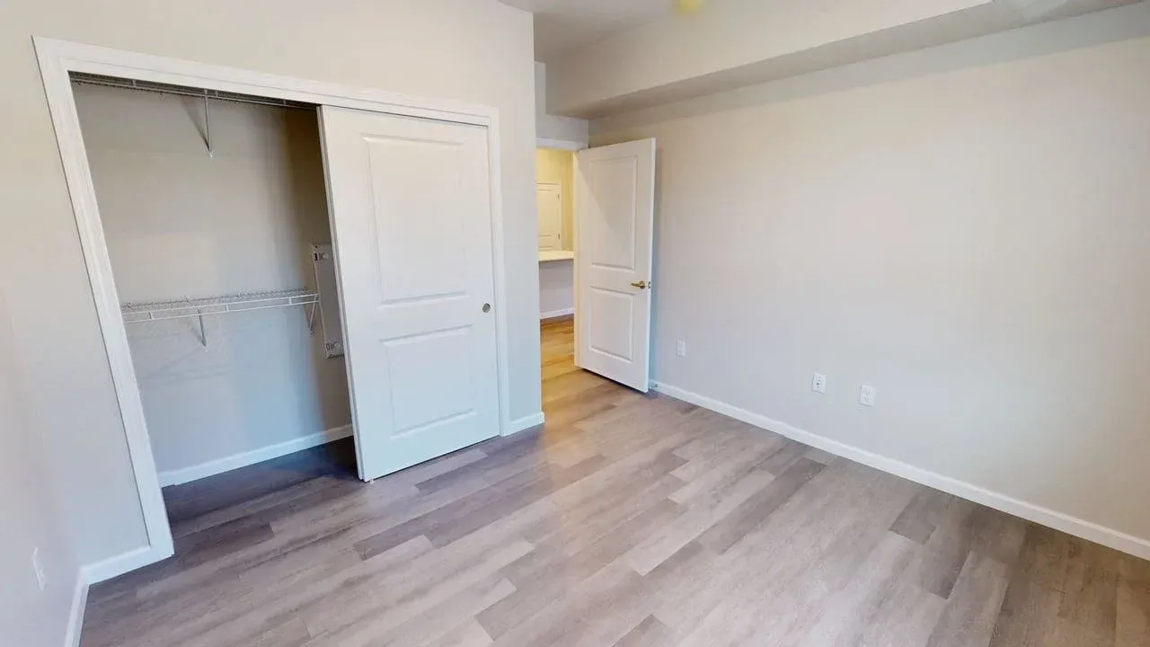 An empty bedroom with hardwood floors and a closet.