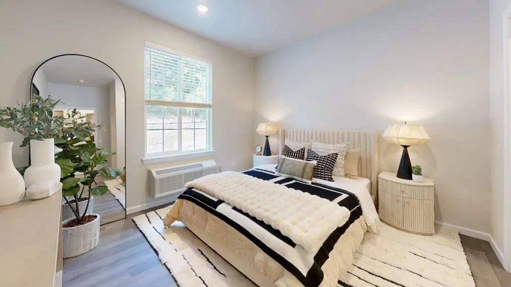 A bedroom with a bed , nightstand , mirror and window.