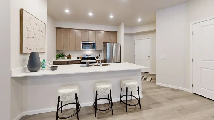A kitchen with a large island , stools and a refrigerator.