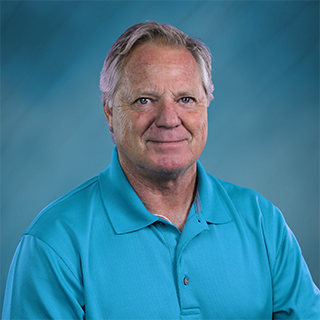 A man in a suit and striped shirt is smiling in front of a blue background.