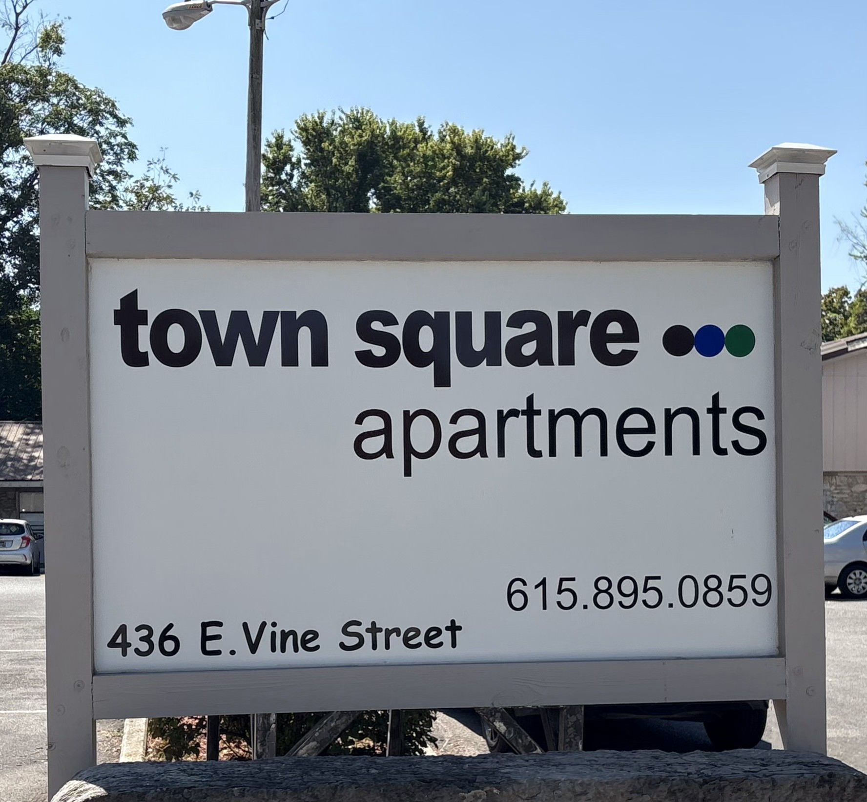 Sign for Town Square Apartments at 436 E. Vine Street. Black text on white background with blue, green, and black dots.
