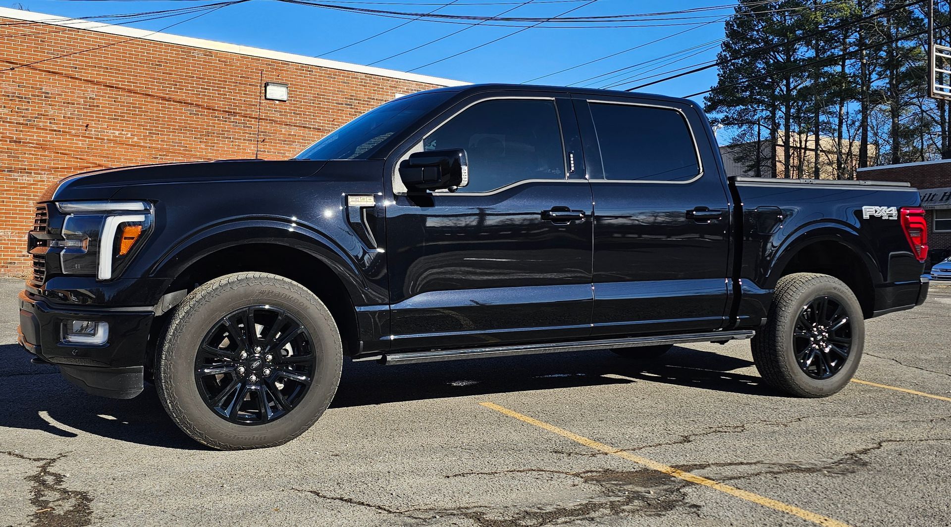 Black Ford F-150 pickup truck parked in front of a brick building. Dark tinted windows and black wheels.