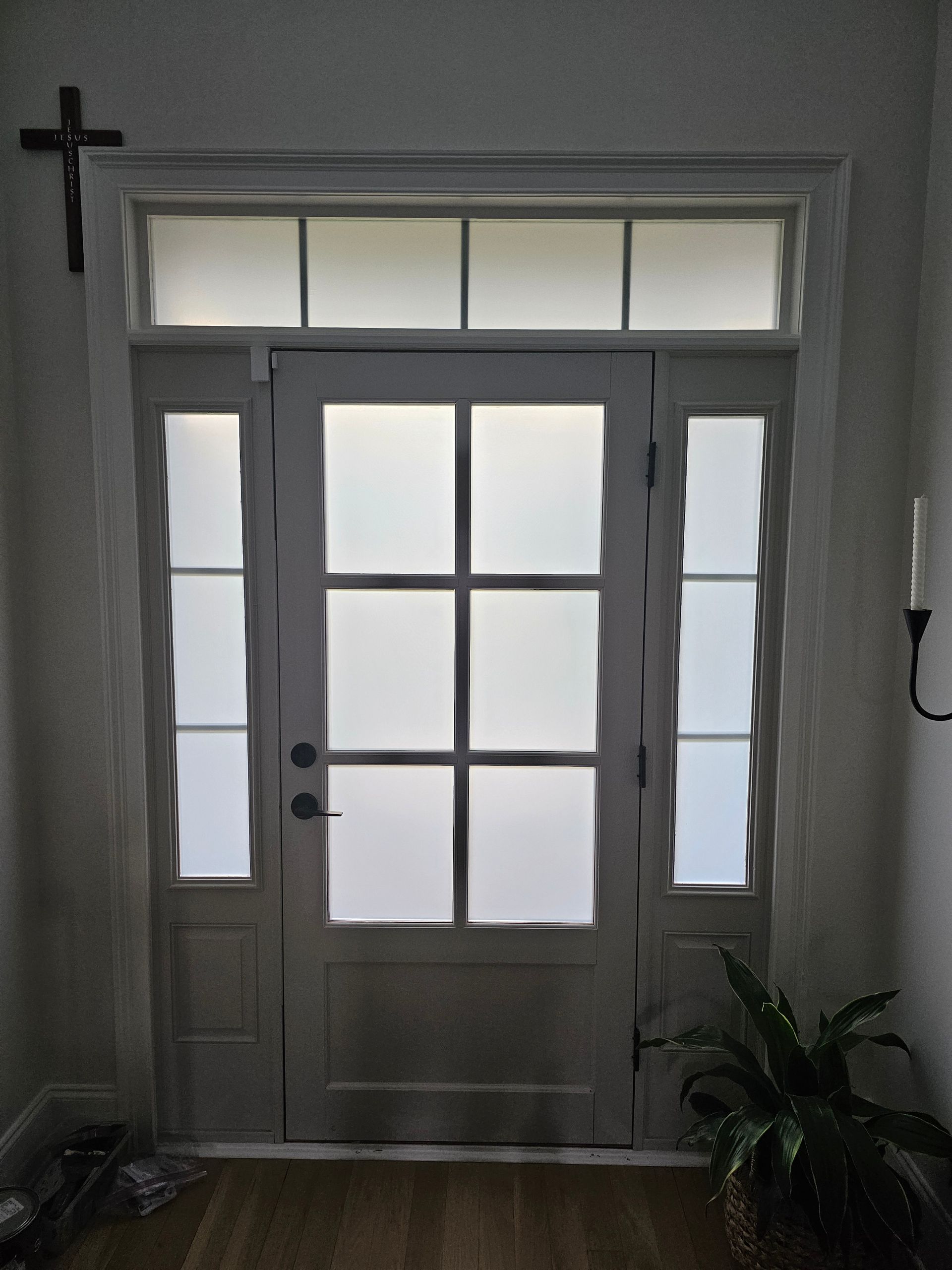 White front door with sidelights, transom, and cross, inside a building.