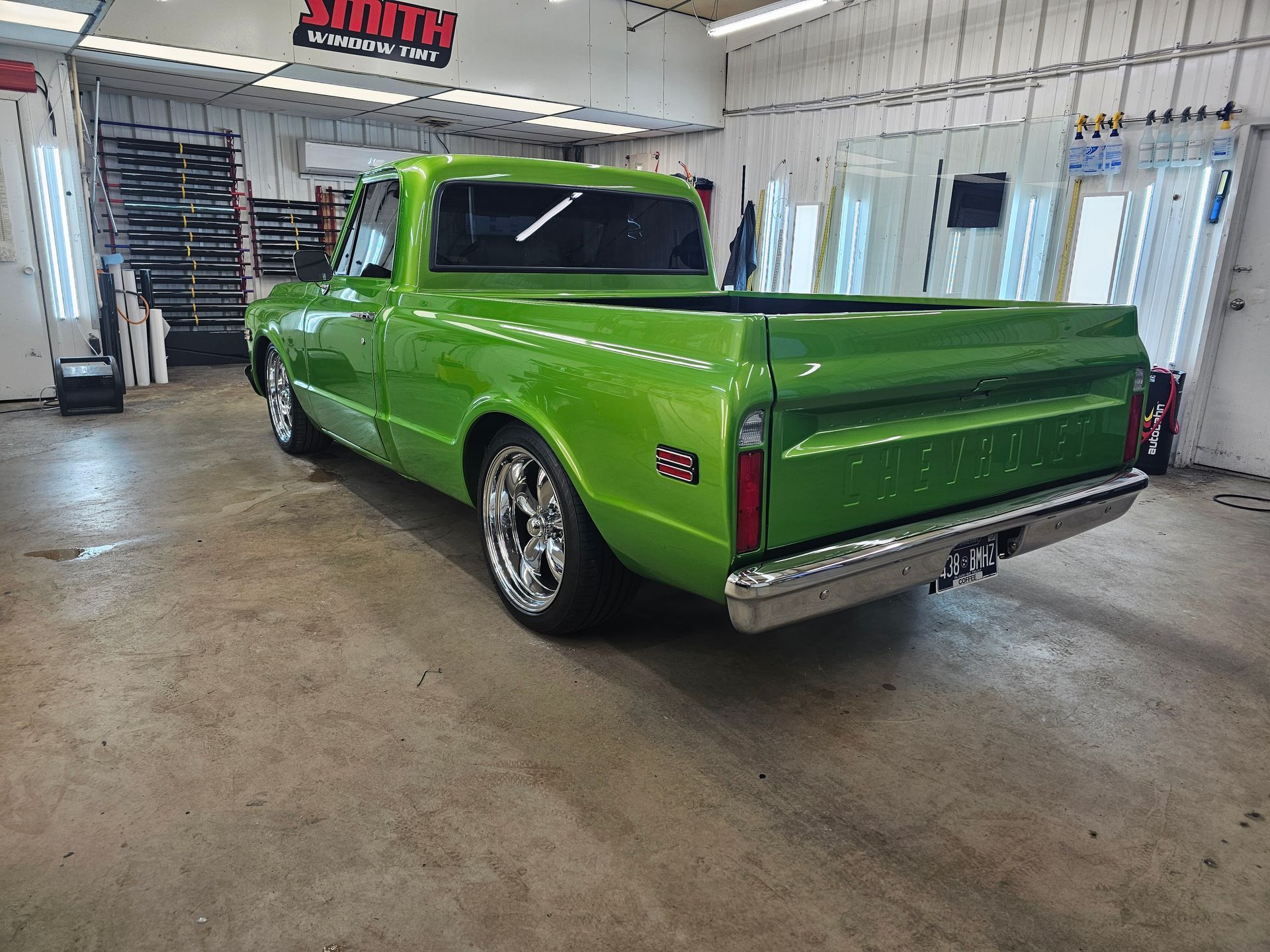 Green classic pickup truck in a garage with chrome wheels.