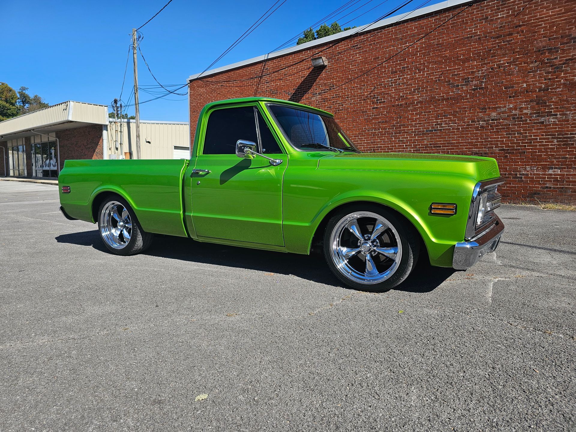 Bright green classic pickup truck parked on pavement in front of a brick building.