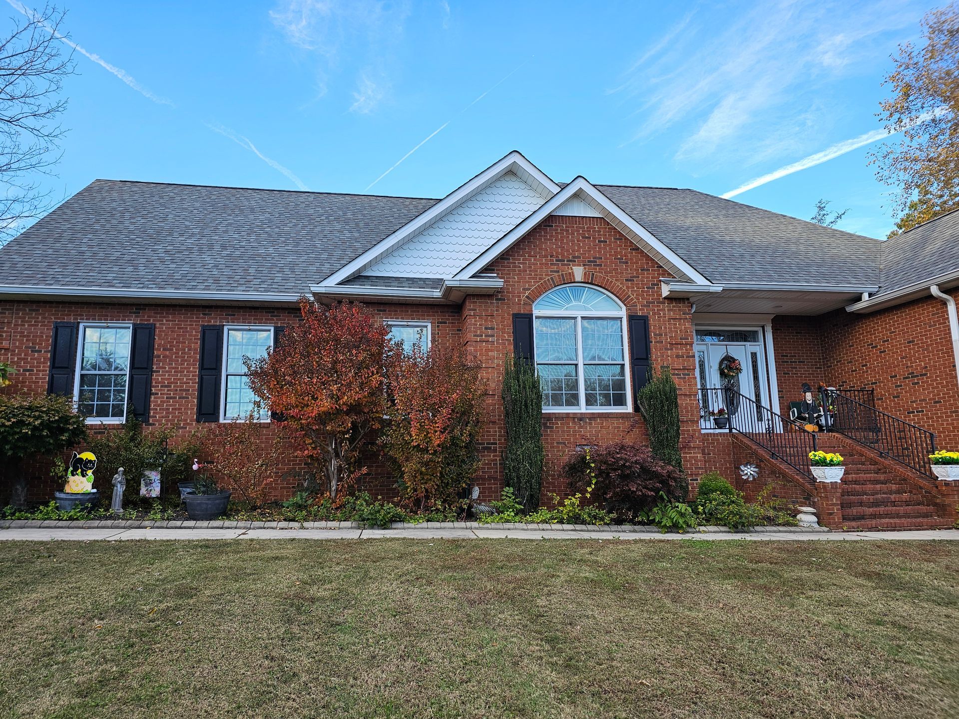 Red brick house with dark shutters, arched window, and front steps with fall decorations.