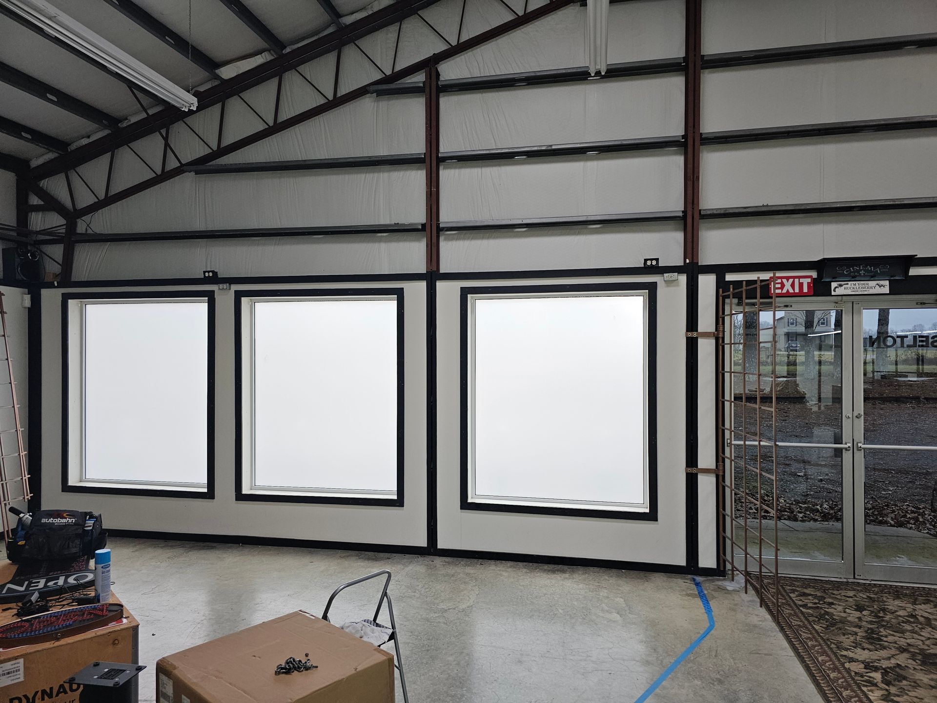 Interior of a commercial building with three large windows, a door, and exposed metal beams.