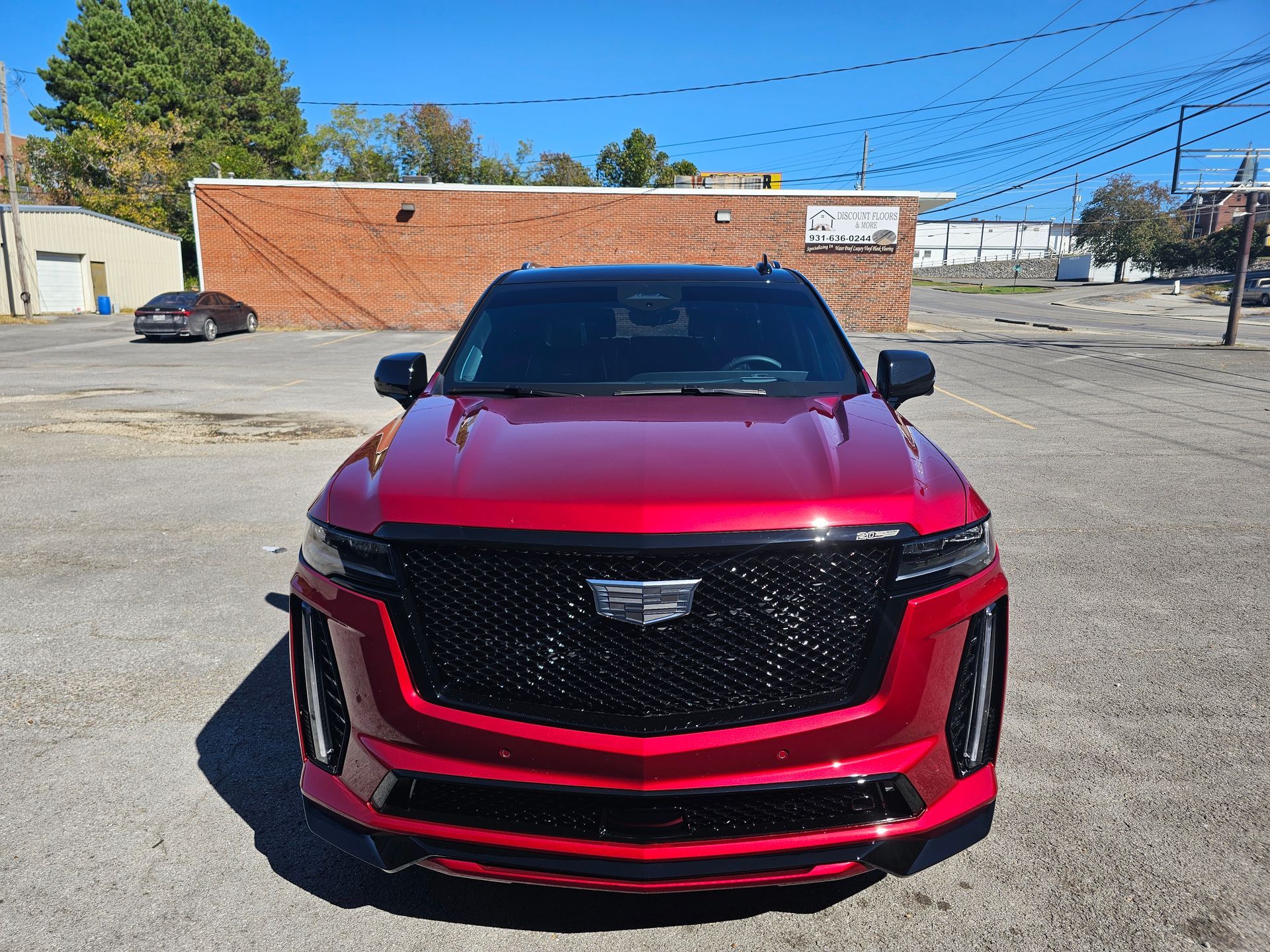 A red cadillac escalade is parked in a parking lot in front of a brick building.