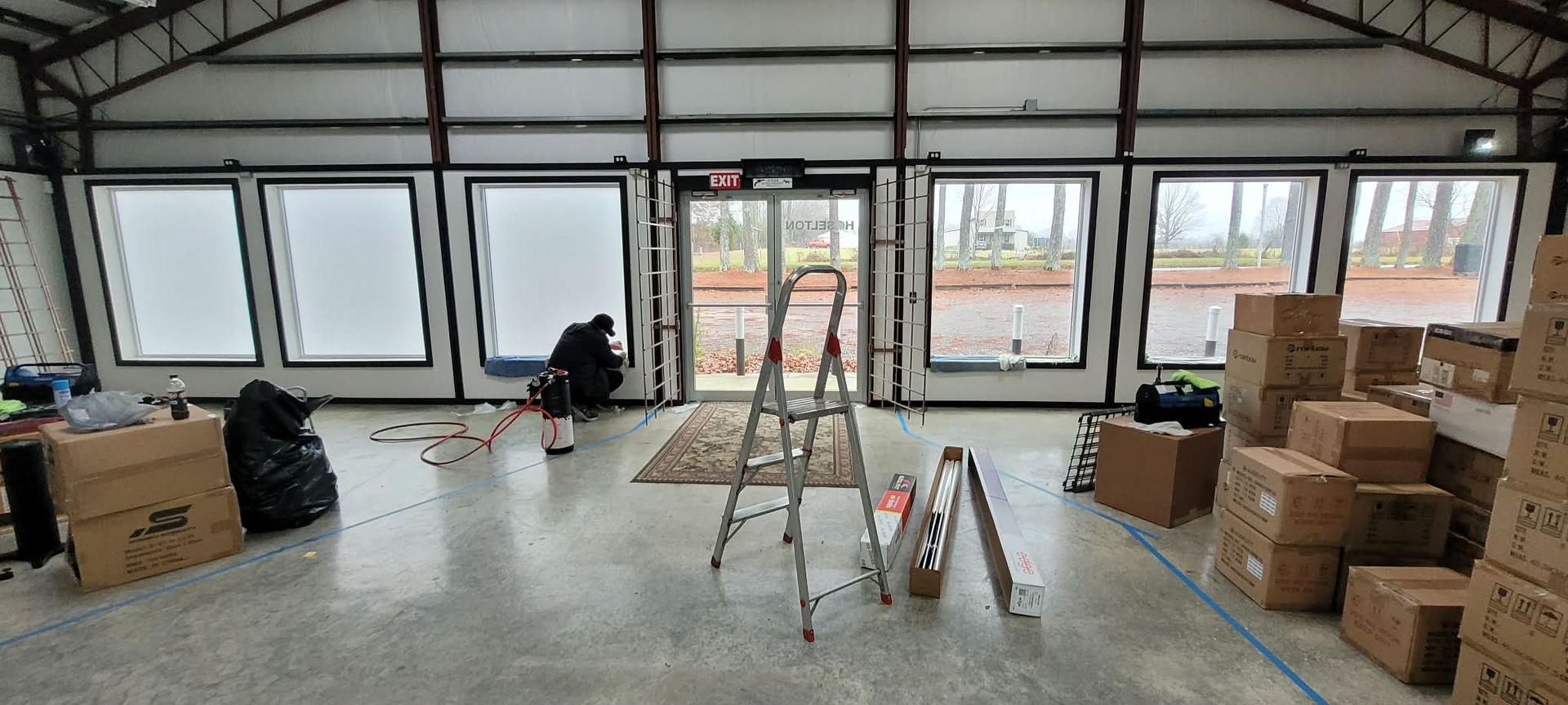 A large interior space with windows, a person working, and boxes stacked.