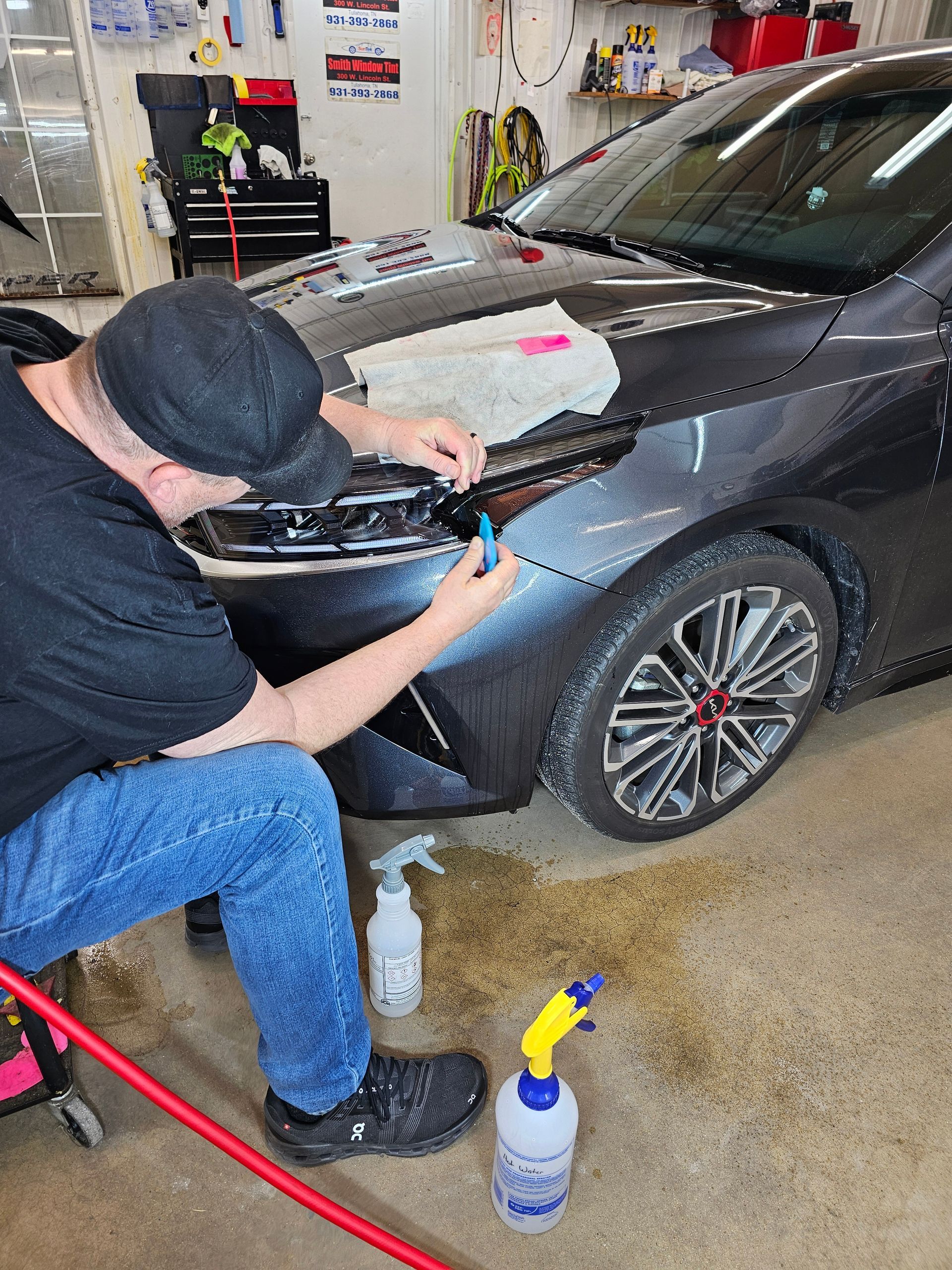 A man is sitting in front of a car in a garage.